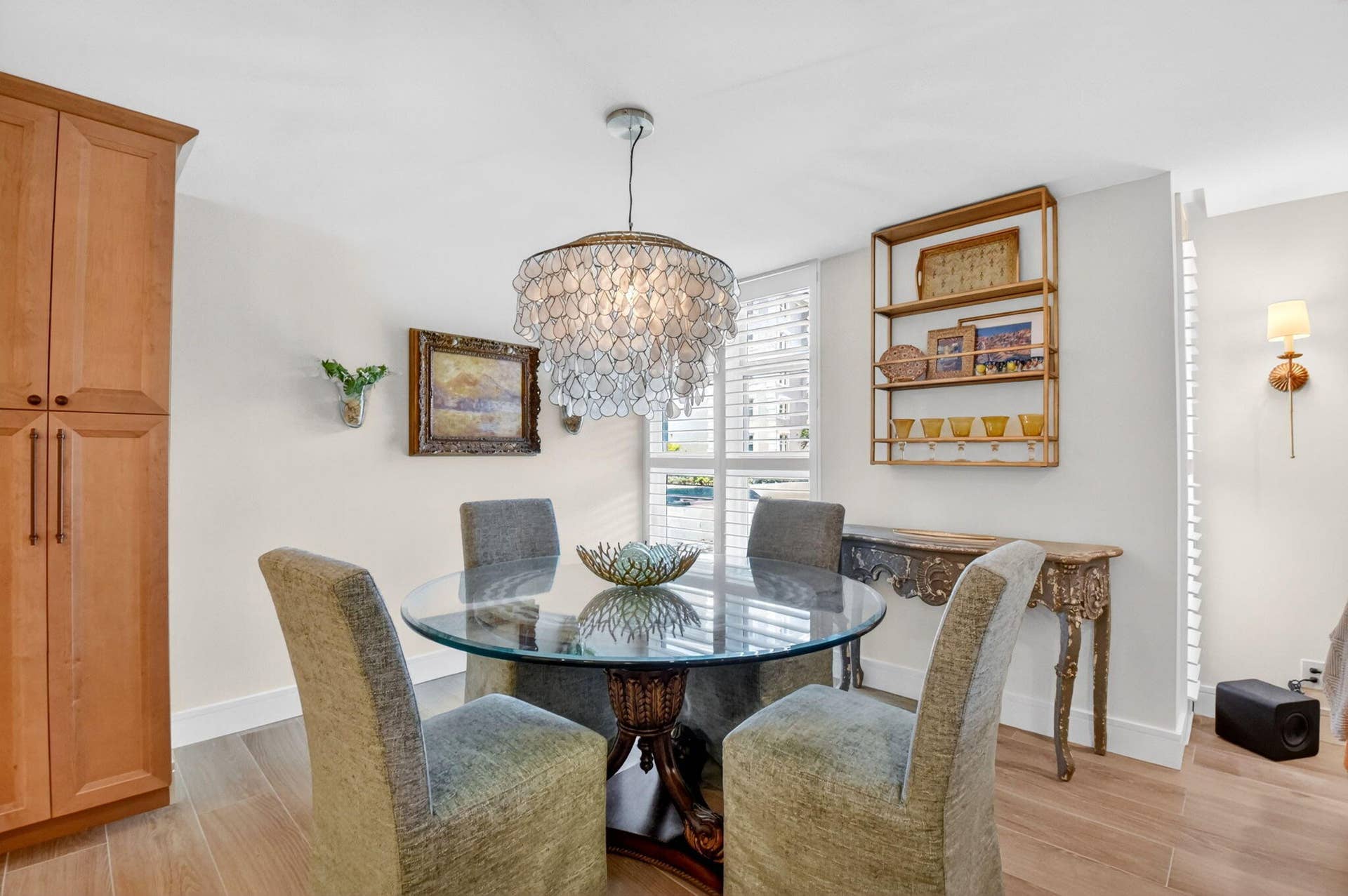 Wood-finish flooring, floor-to-ceiling wooden storage cabinetry, ornamental tiered chandelier, custom wall-mounted sconce, and plantation shutters