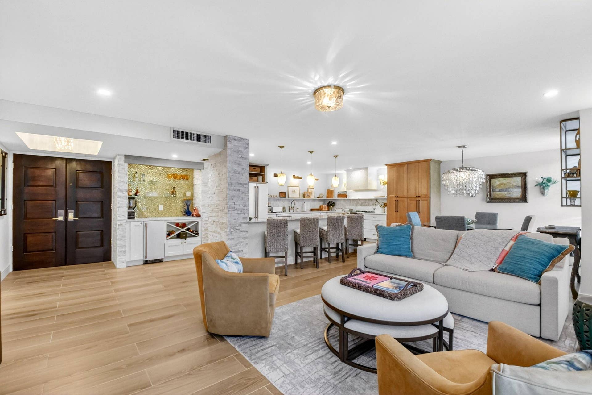 Open floor plan featuring wood-finish flooring, a built-in wet bar with stone-accented columns, a kitchen island with pendant lighting, and recessed ceiling illumination