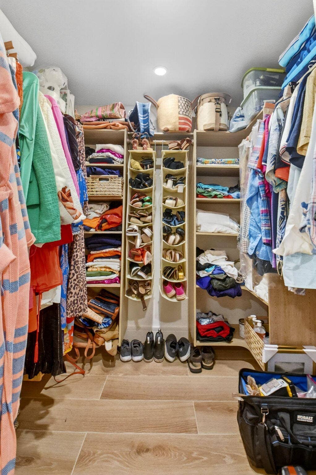 Walk-in closet featuring custom laminate shelving units, overhead recessed lighting, and wood-finish tile flooring