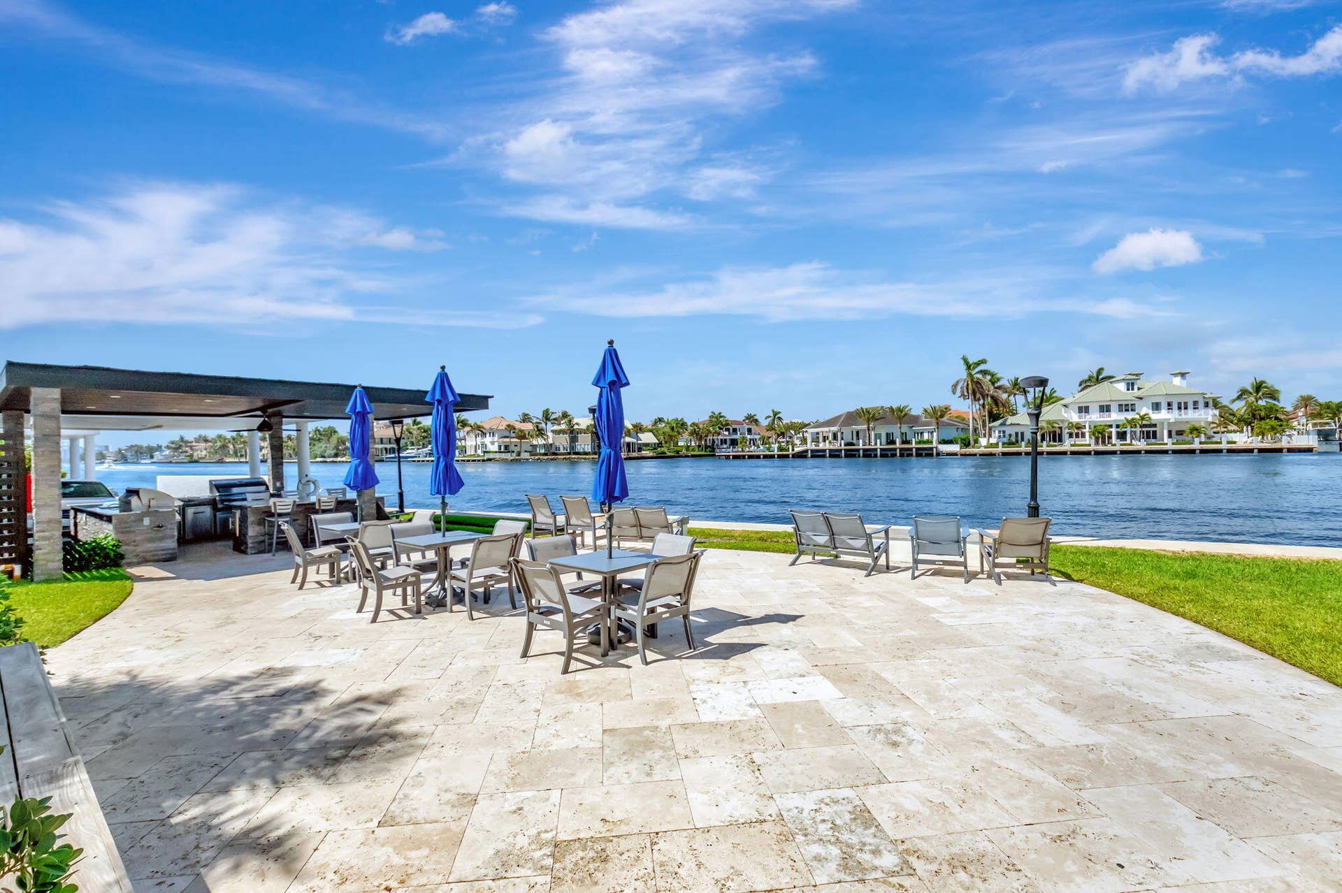 Waterfront patio featuring stone pavers, a covered outdoor kitchen with a built-in grill, and a manicured lawn