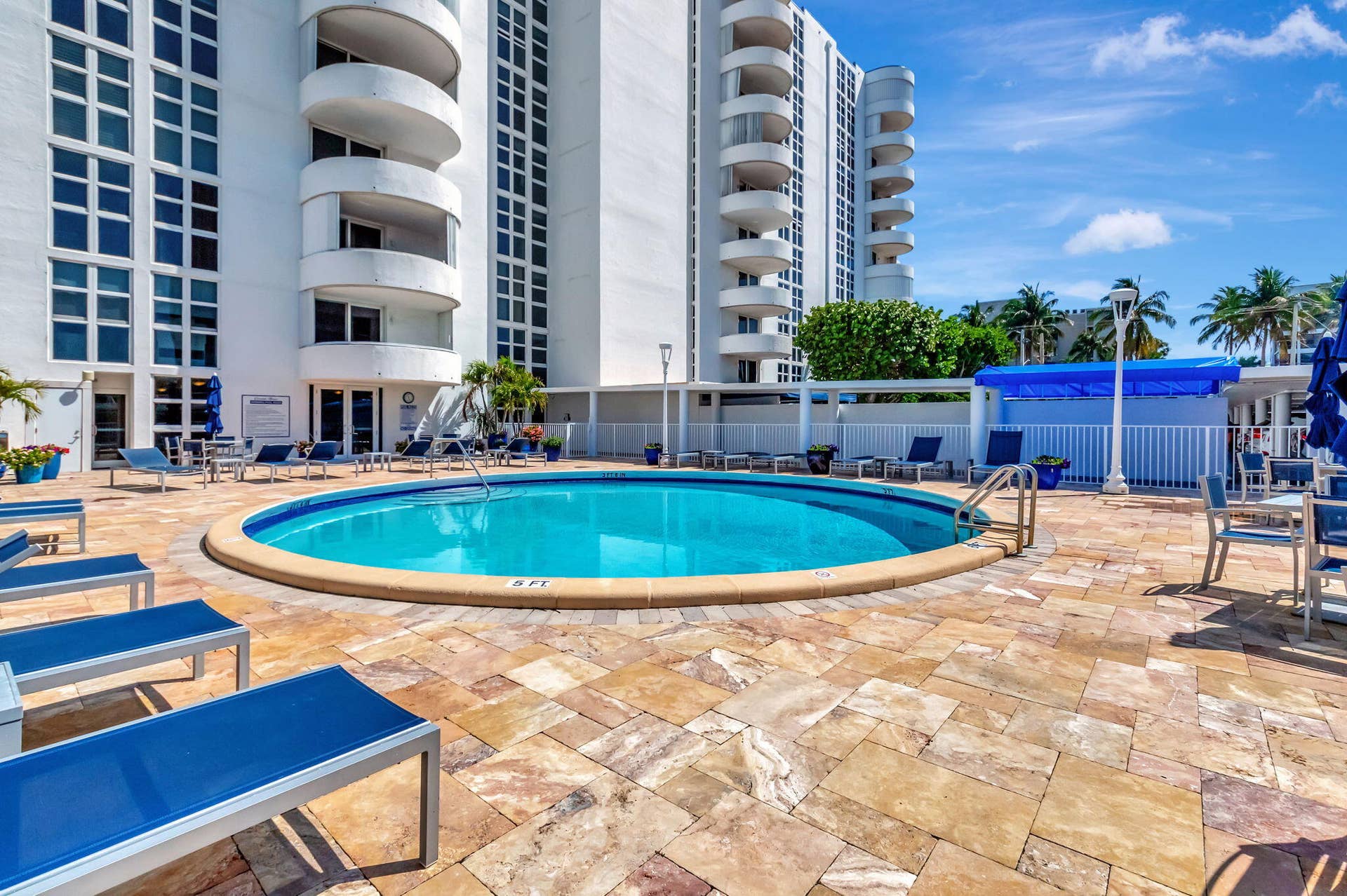 Circular swimming pool set within a paved stone deck, featuring multi-story high-rise architecture with curved balconies