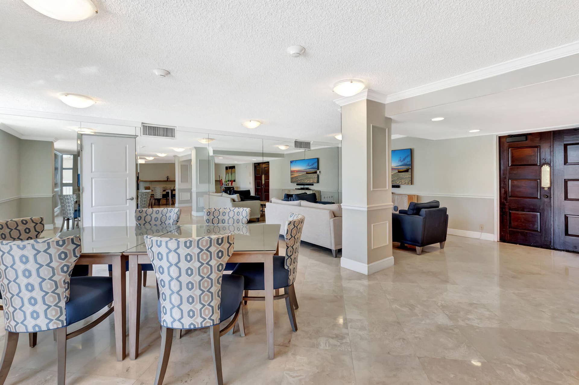 Open-concept interior featuring polished stone flooring, recessed lighting, mirrored wall accents, structural pillars with crown molding, and double wood-paneled entry doors