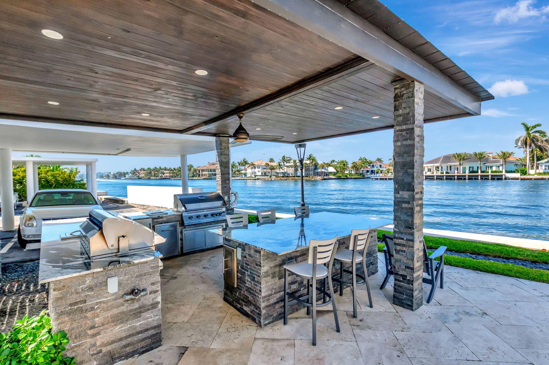 Covered waterfront patio featuring a stone-clad outdoor kitchen, granite-topped island, recessed lighting, and a wood-paneled ceiling