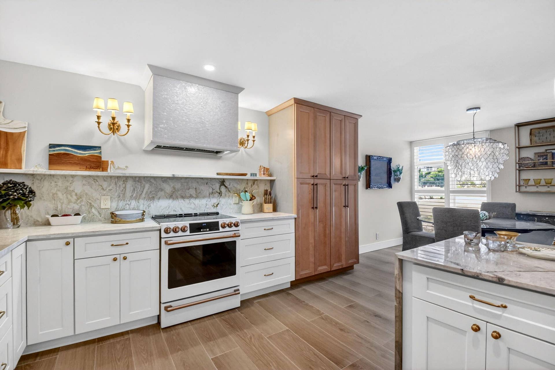 Kitchen featuring white shaker-style cabinetry, natural stone countertops with matching backsplash, wood-finish flooring, built-in floor-to-ceiling pantry storage, and a custom range hood