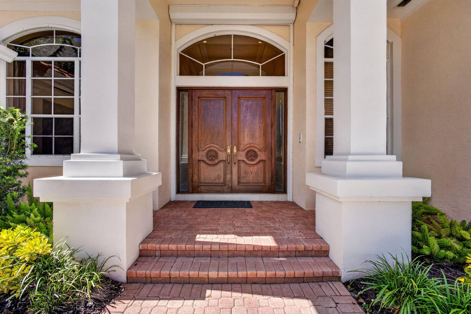 42 Windward Isle, Palm Beach Gardens, FL 33418 Double wood-paneled front doors with carved detail, arched transom window, brick masonry entry steps, and structural square columns