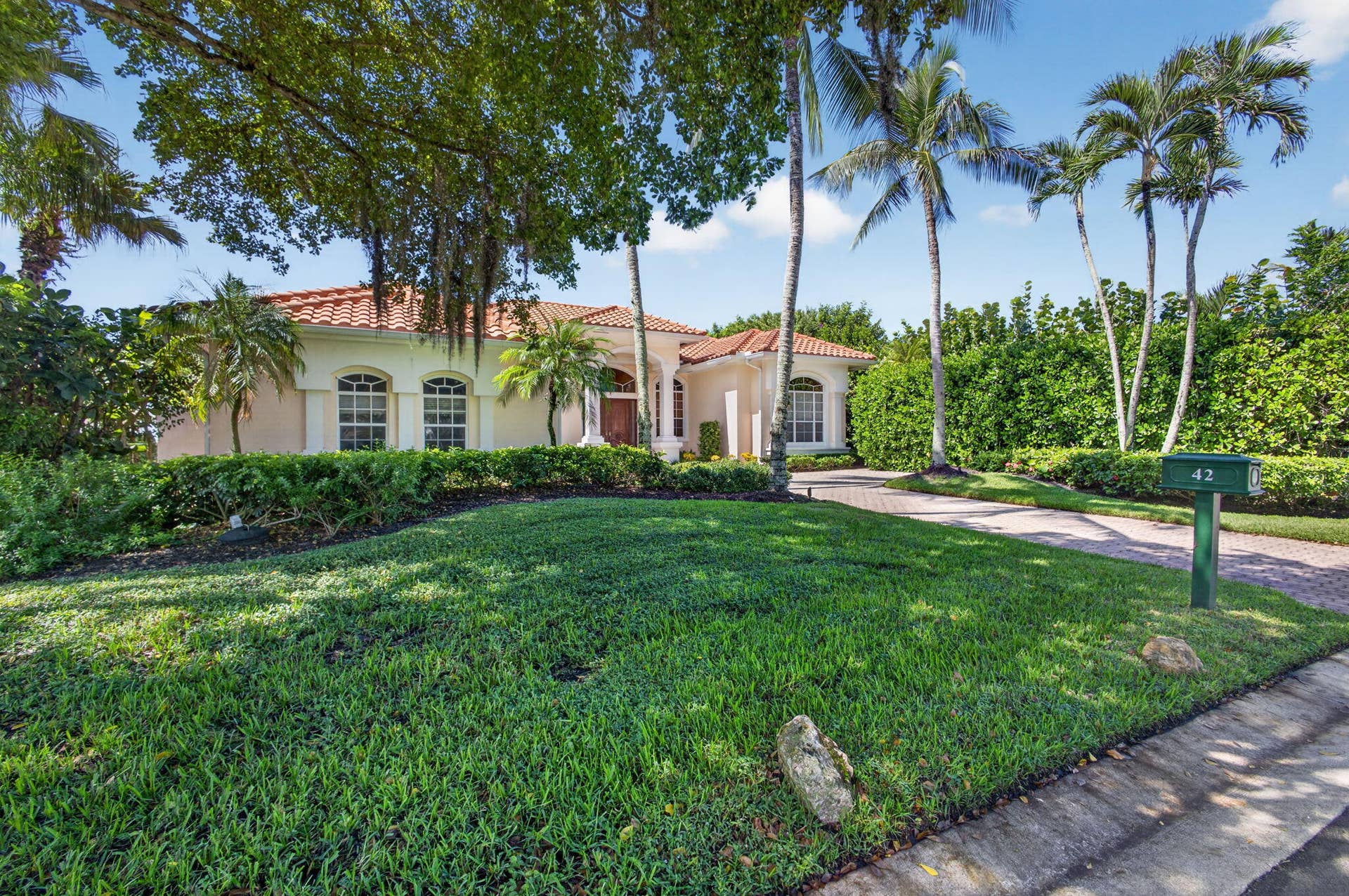 42 Windward Isle, Palm Beach Gardens, FL 33418 Single-story residence featuring a tile roof, arched windows, decorative columns, and a paved driveway