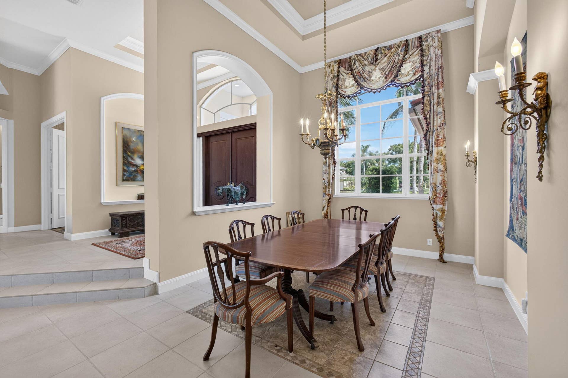 42 Windward Isle, Palm Beach Gardens, FL 33418 Dining area featuring high ceilings, crown molding, arched architectural wall cutouts, a custom-installed chandelier, and large windows with transom detail