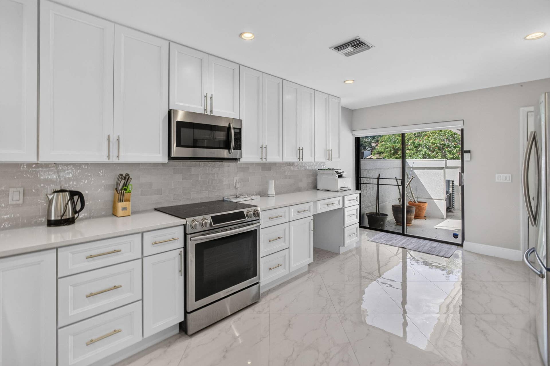 543 Prestwick Circle, Palm Beach Gardens, FL 33418 Kitchen featuring white shaker-style cabinetry, quartz countertops, stainless steel appliances, a textured tile backsplash, and polished stone-finish flooring