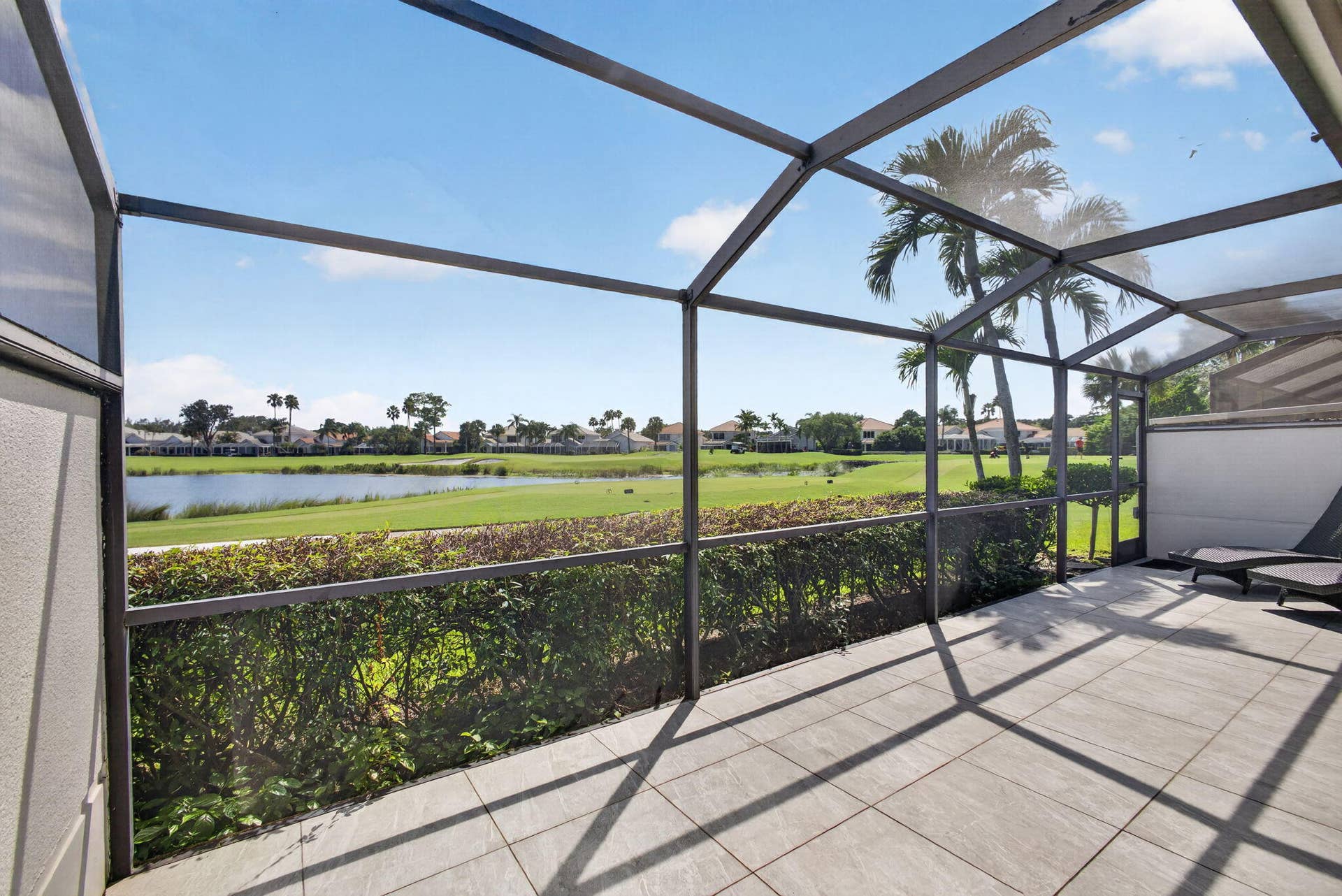 543 Prestwick Circle, Palm Beach Gardens, FL 33418 Screened-in lanai featuring large-format tile flooring and an metal structural frame, overlooking a pond, manicured lawn, and mature palm trees