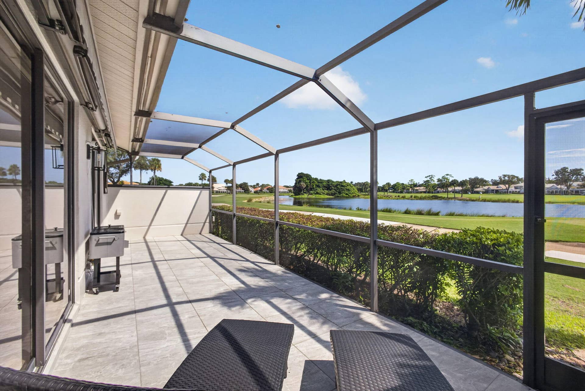 543 Prestwick Circle, Palm Beach Gardens, FL 33418 Screened-in patio with large-format tile flooring, metal frame enclosure, and exterior lighting, featuring a water and golf course backdrop