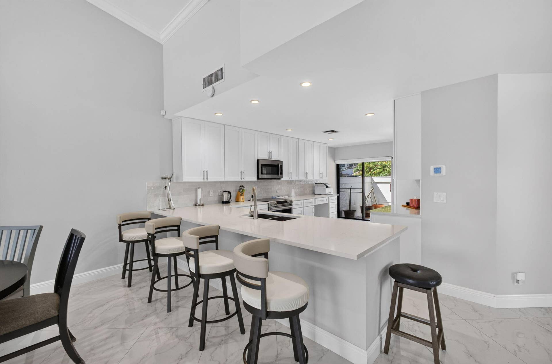543 Prestwick Circle, Palm Beach Gardens, FL 33418 Kitchen featuring white shaker-style cabinetry, quartz countertops, a peninsula with bar seating, integrated stainless steel appliances, and large-format tile flooring