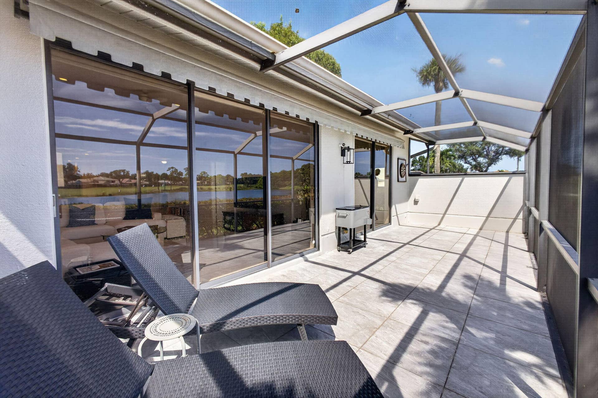 543 Prestwick Circle, Palm Beach Gardens, FL 33418 Screened-in lanai featuring large-format tile flooring, a metal frame enclosure, sliding glass doors, and wall-mounted exterior lighting