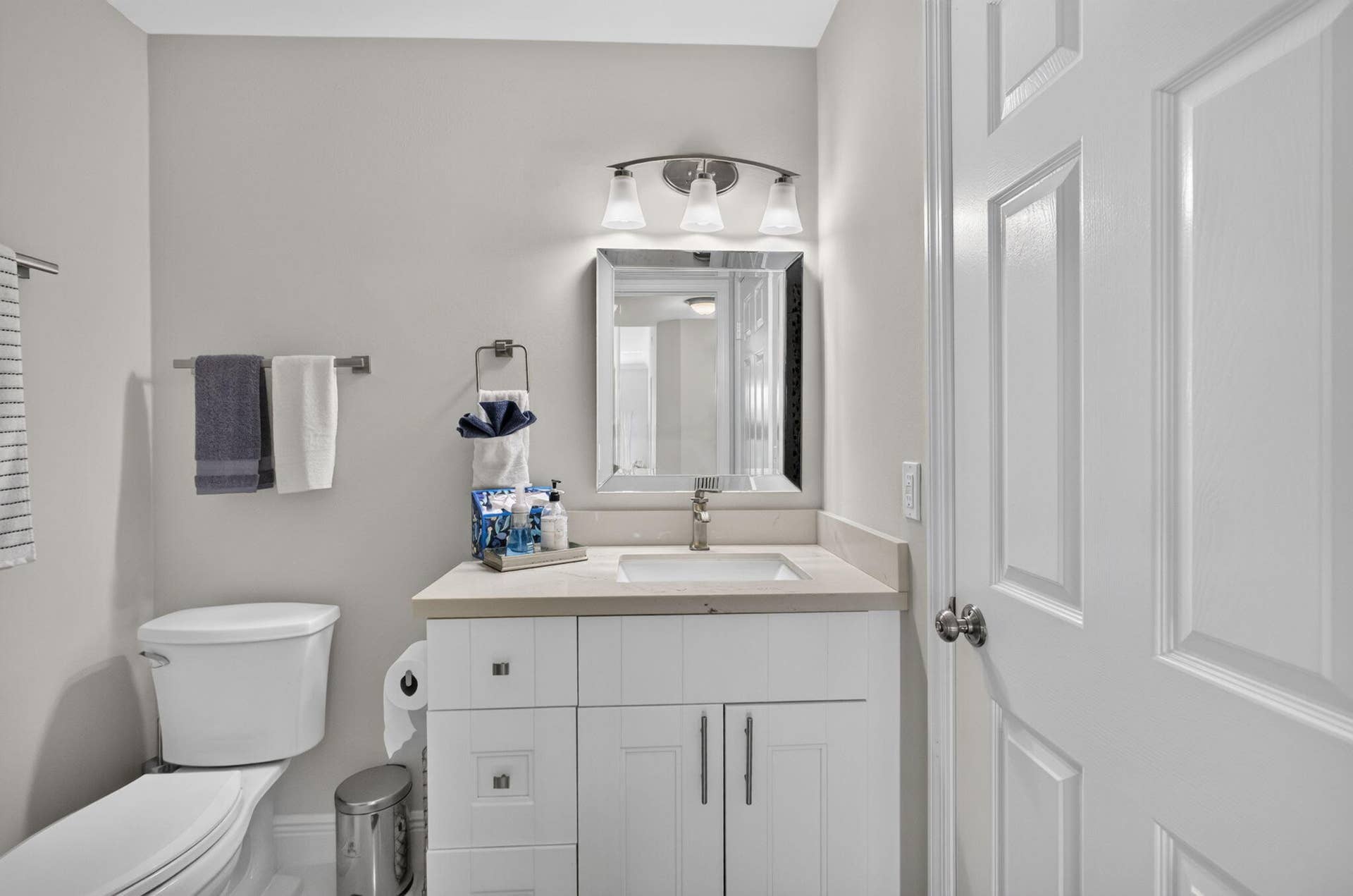 543 Prestwick Circle, Palm Beach Gardens, FL 33418 White cabinetry vanity featuring a stone countertop, integrated sink, brushed metal hardware, and a framed mirror with a triple-light fixture