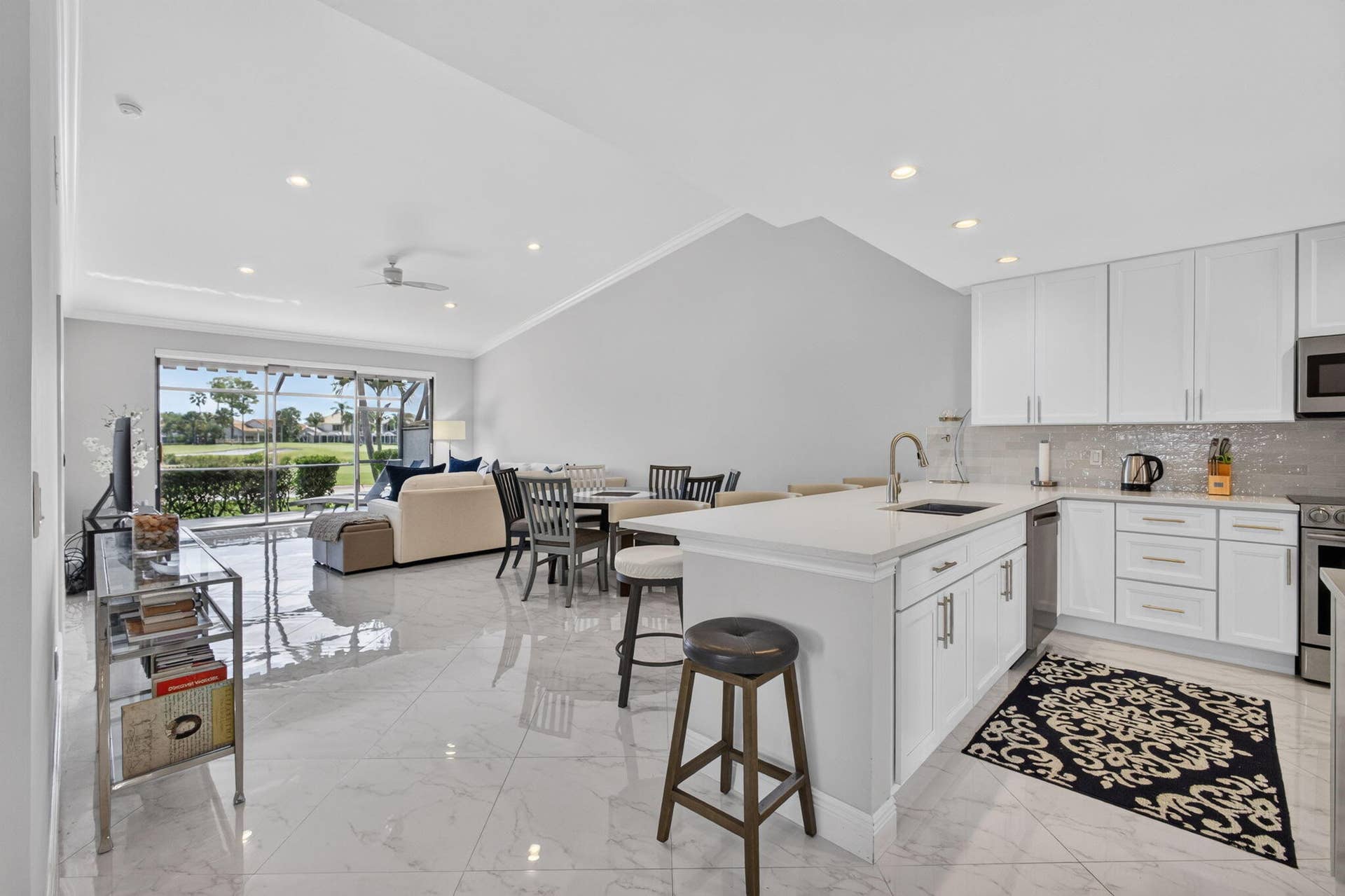 543 Prestwick Circle, Palm Beach Gardens, FL 33418 Open-concept interior featuring vaulted ceilings, light-tone tile flooring, and a kitchen equipped with white shaker cabinetry, quartz countertops, and stainless steel appliances