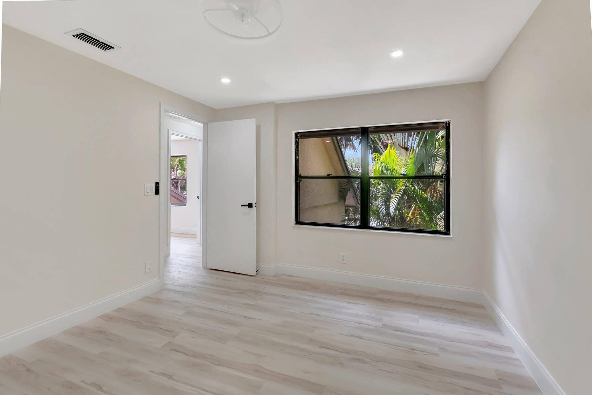 Neutral-toned interior featuring wood-finish flooring, recessed lighting, a single-pane window with black framing, and a door with matte black hardware