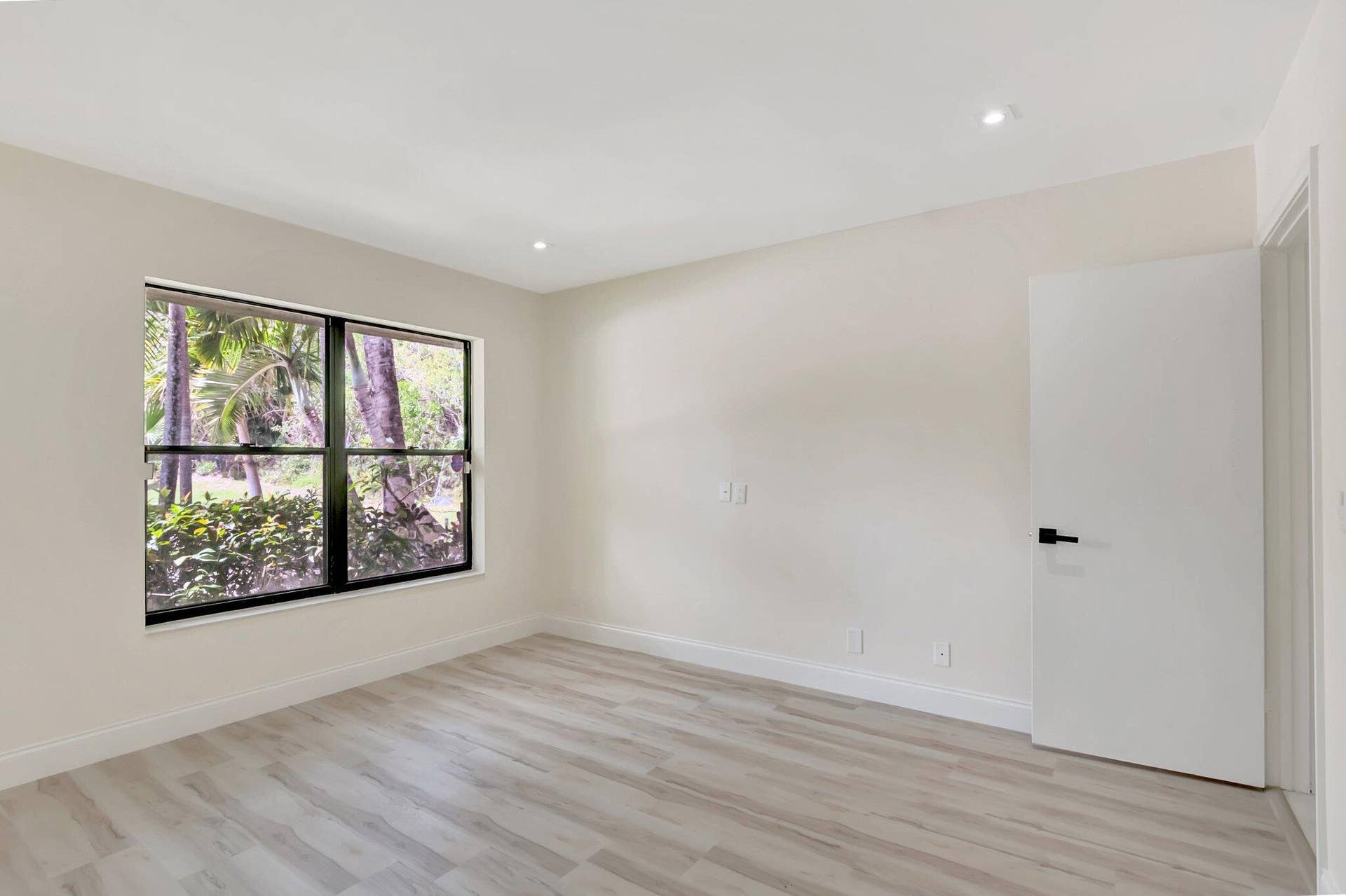 Interior space featuring wood-finish flooring, recessed lighting, a large window with a dark frame, and a solid-panel door with matte black hardware
