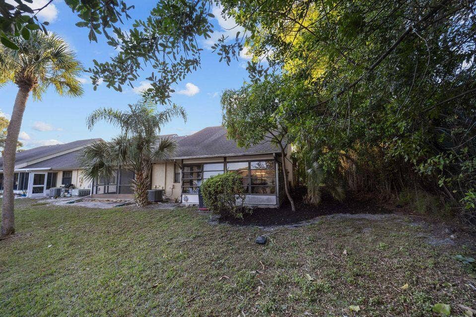 Exterior area featuring a screened-in lanai, mature palm trees, established landscaping, and a sloped shingle roofline