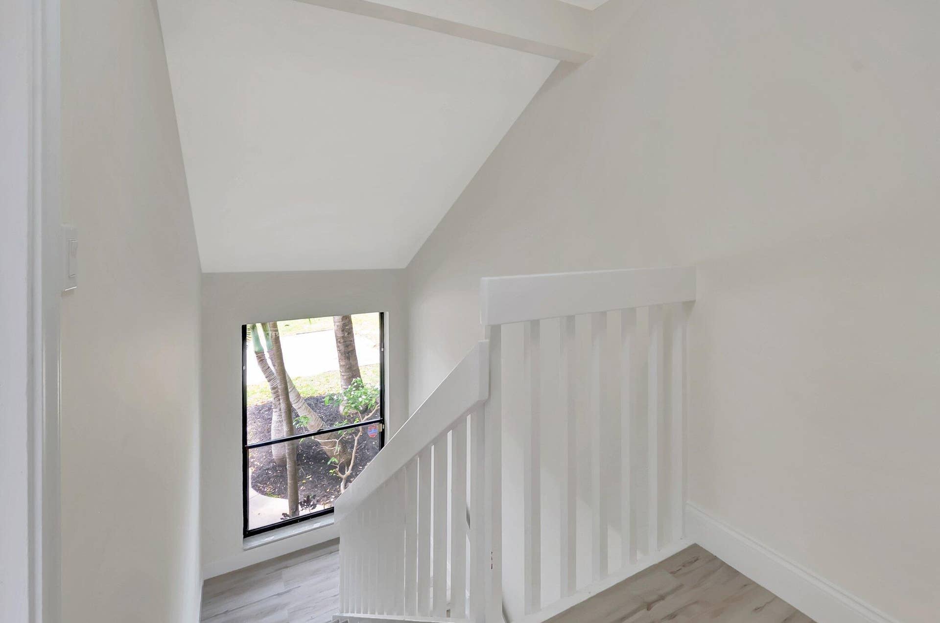 Stairwell featuring white vertical balusters, wood-finish flooring, vaulted ceiling, and a black-framed window