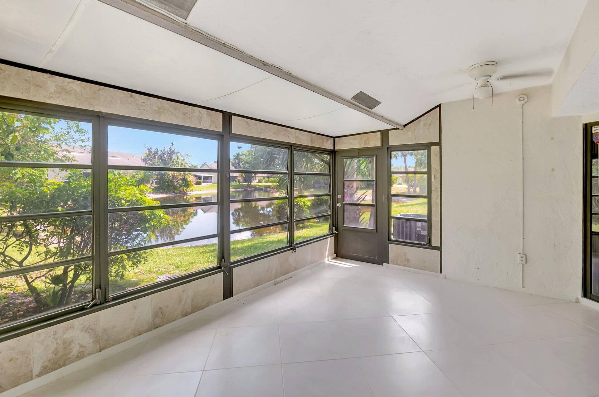 Enclosed patio featuring floor-to-ceiling screened windows, large-format tile flooring, stone-tiled wall accents, and an integrated ceiling fan