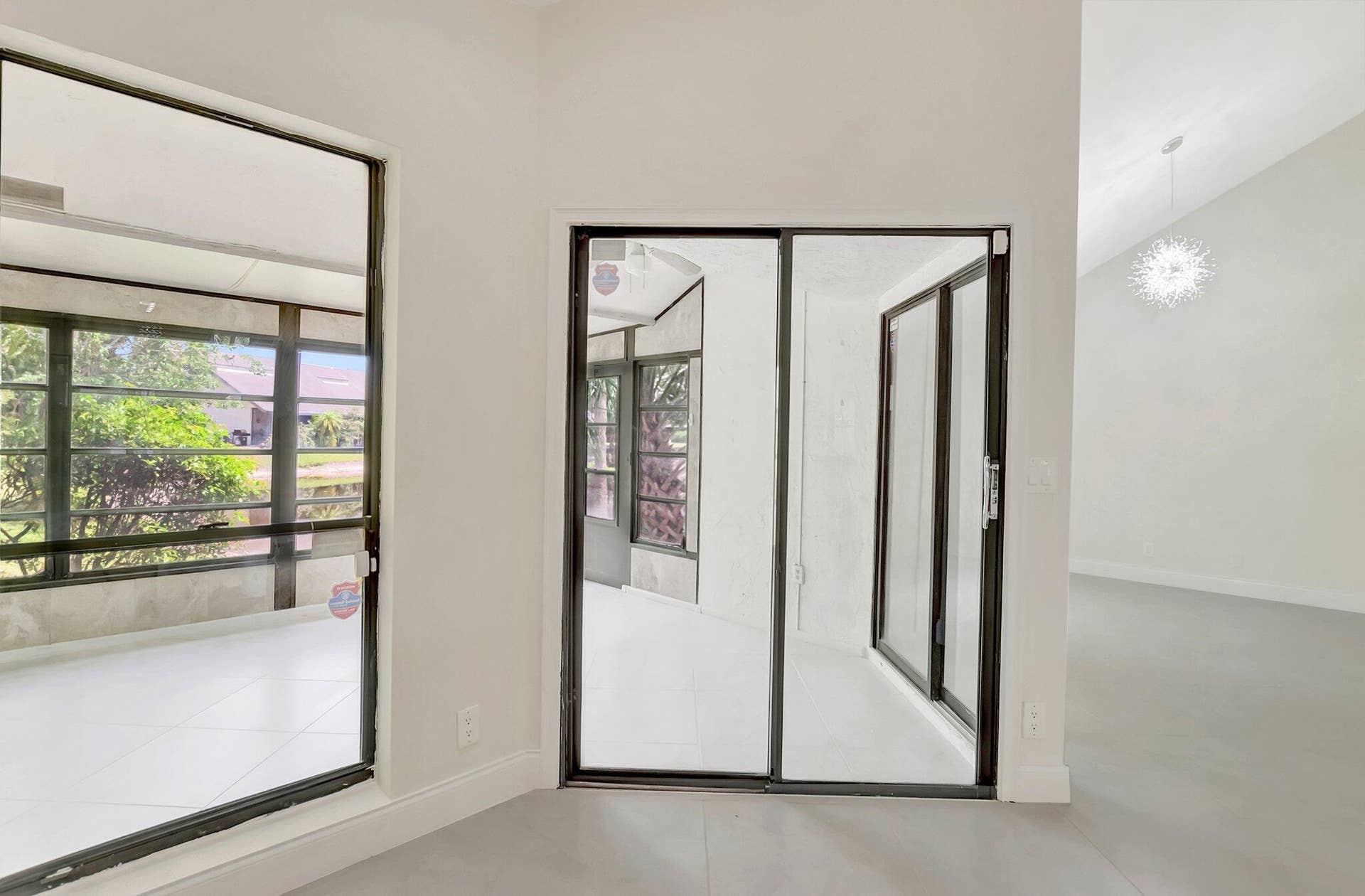 Sliding glass doors with dark frames, large-format tile flooring, vaulted ceilings, and decorative pendant lighting