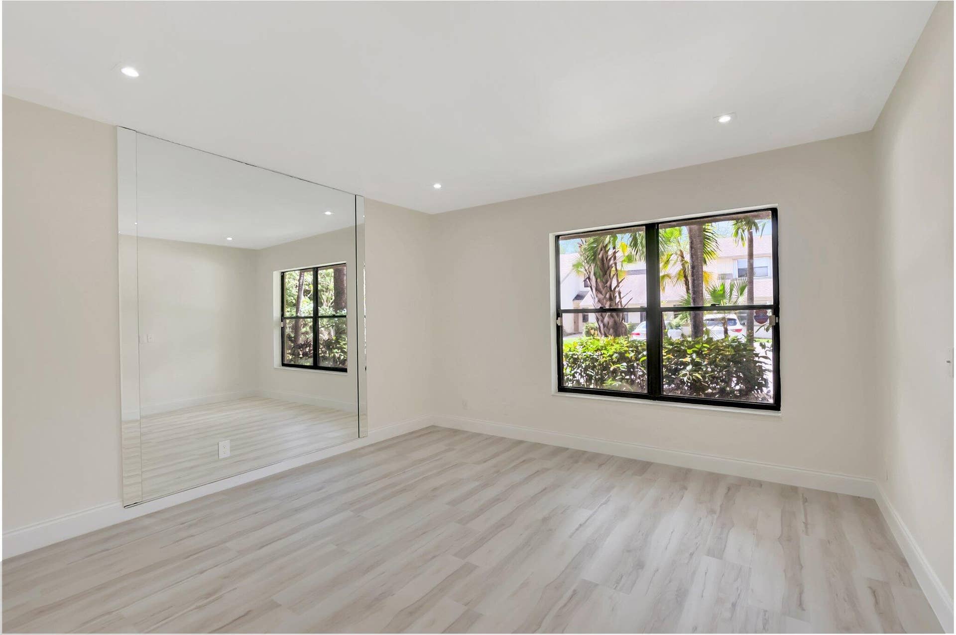 Room featuring wood-finish flooring, recessed lighting, expansive wall mirror, and large windows with black frames
