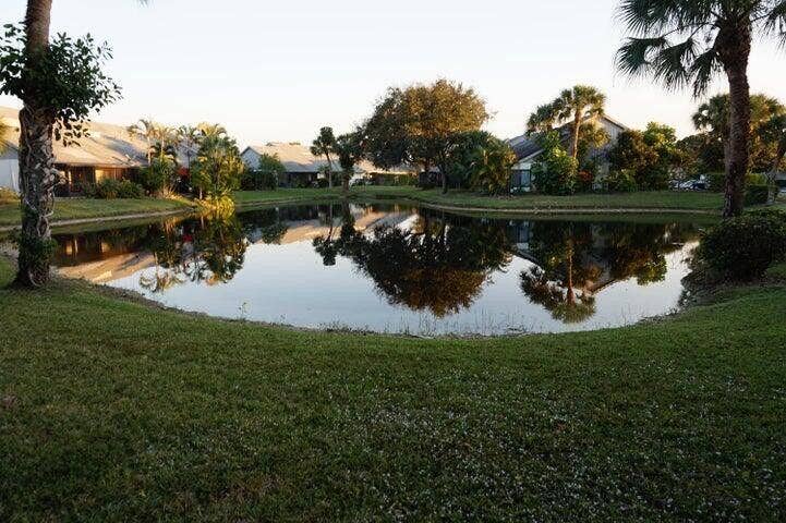 Waterfront parcel featuring a natural pond, manicured lawn, and mature palm trees