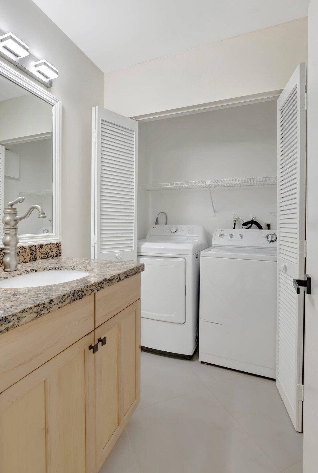 Vanity with stone-finish countertop, undermount sink, multi-light fixture, and built-in closet with louvered doors