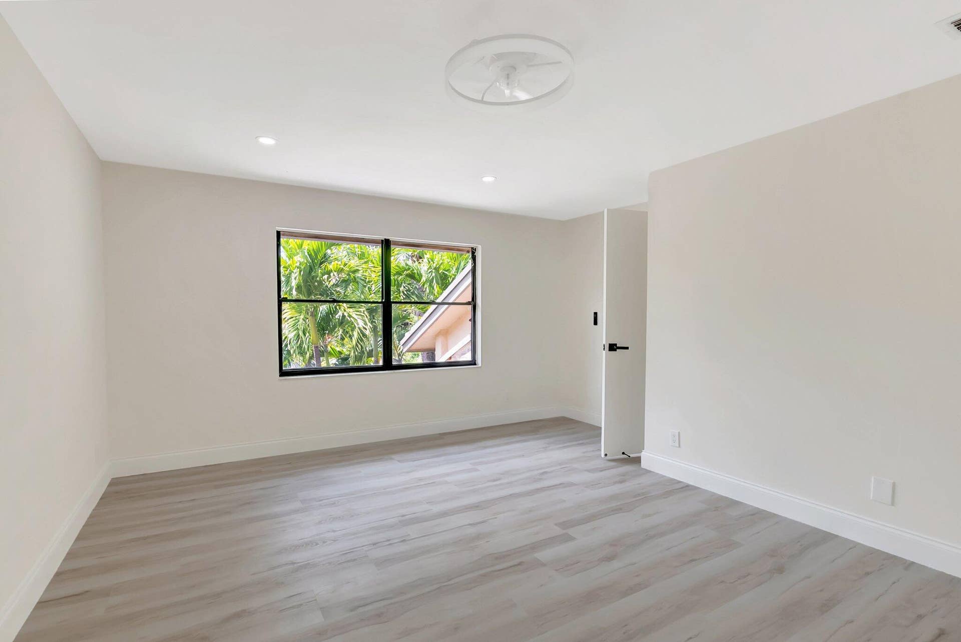 Neutral-toned interior room featuring wood-finish flooring, recessed lighting, a ceiling fan, and a large window with black framing