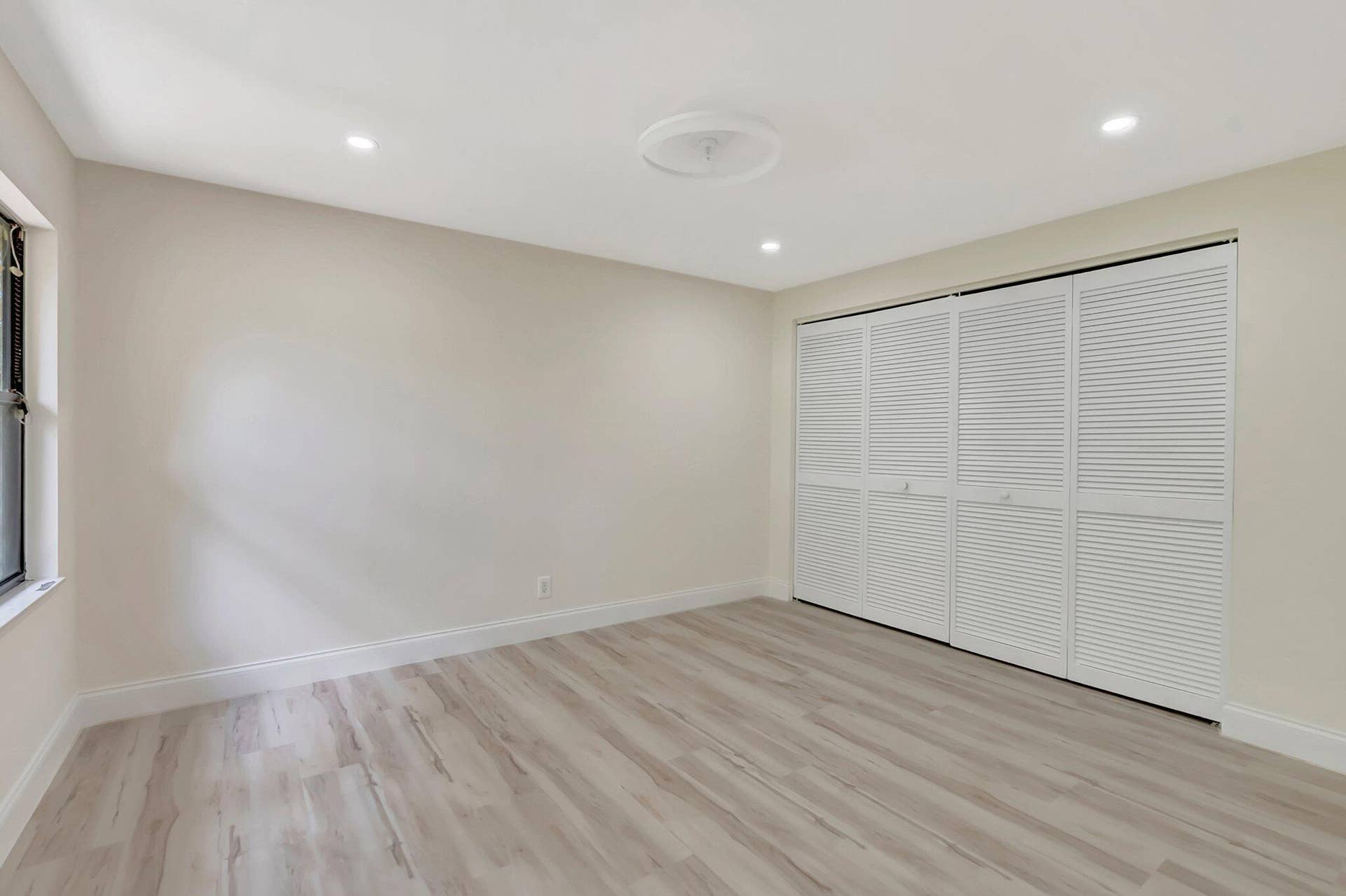 Room featuring wood-finish flooring, recessed lighting, neutral wall tones, and floor-to-ceiling louvered bi-fold closet doors