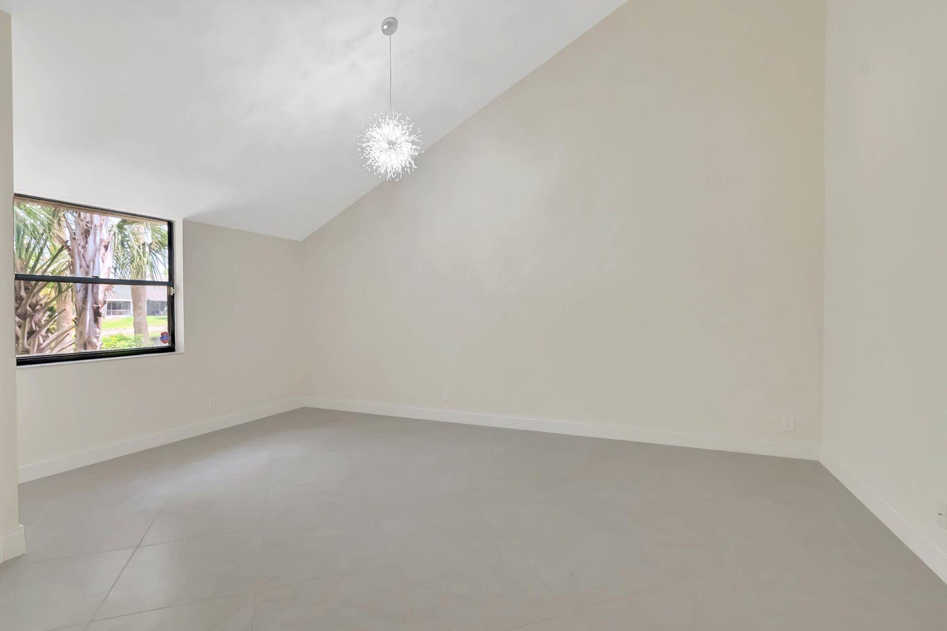 Vaulted ceiling featuring a decorative sputnik-style pendant light, neutral wall finishes, large-format tile flooring, and a window with exterior greenery
