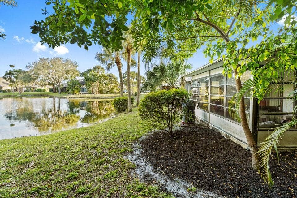 Waterfront lot featuring a screened-in lanai, mature landscaping, and an expansive lawn