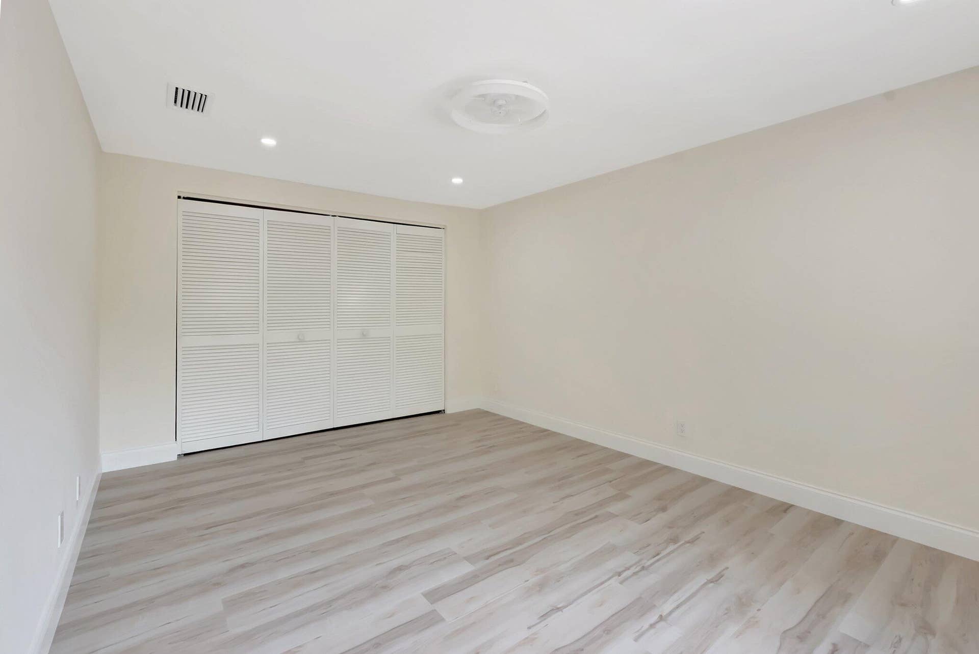 Neutral-toned interior space featuring light wood-finish flooring, recessed ceiling lighting, and a white bi-fold closet door