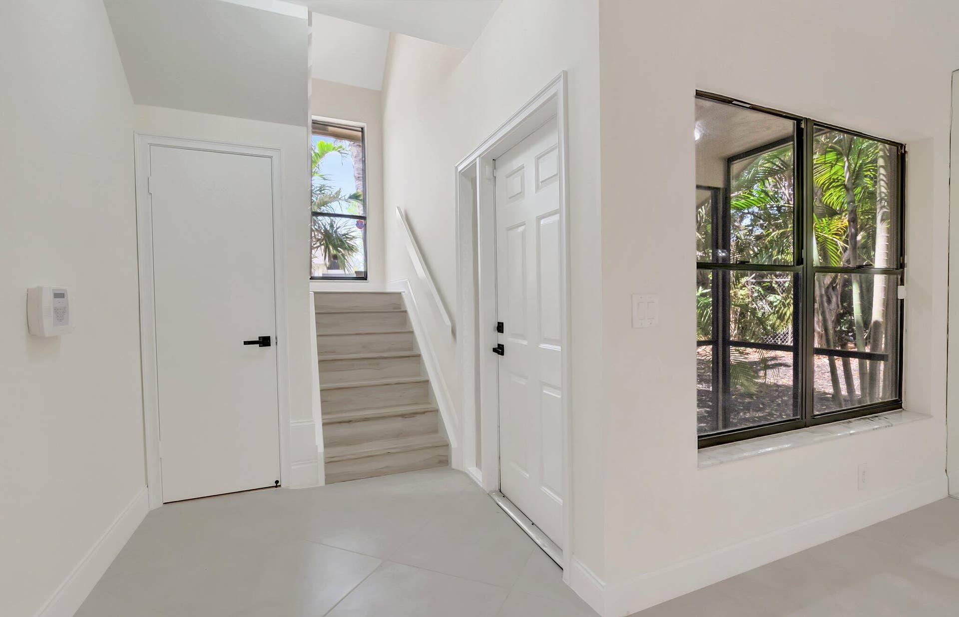 Entryway featuring light-toned tile flooring, wood-finish stairs with a white handrail, large windows, and matte black door hardware