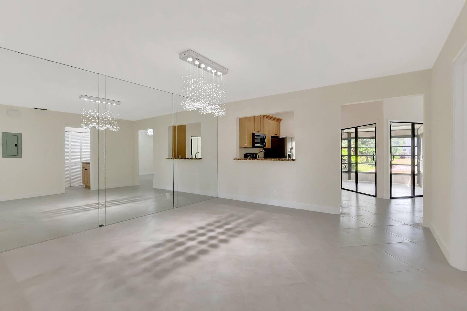 Large-format mirror wall with a crystal-accented chandelier, expansive tile flooring, pass-through kitchen opening, and multi-pane black-frame glass doors