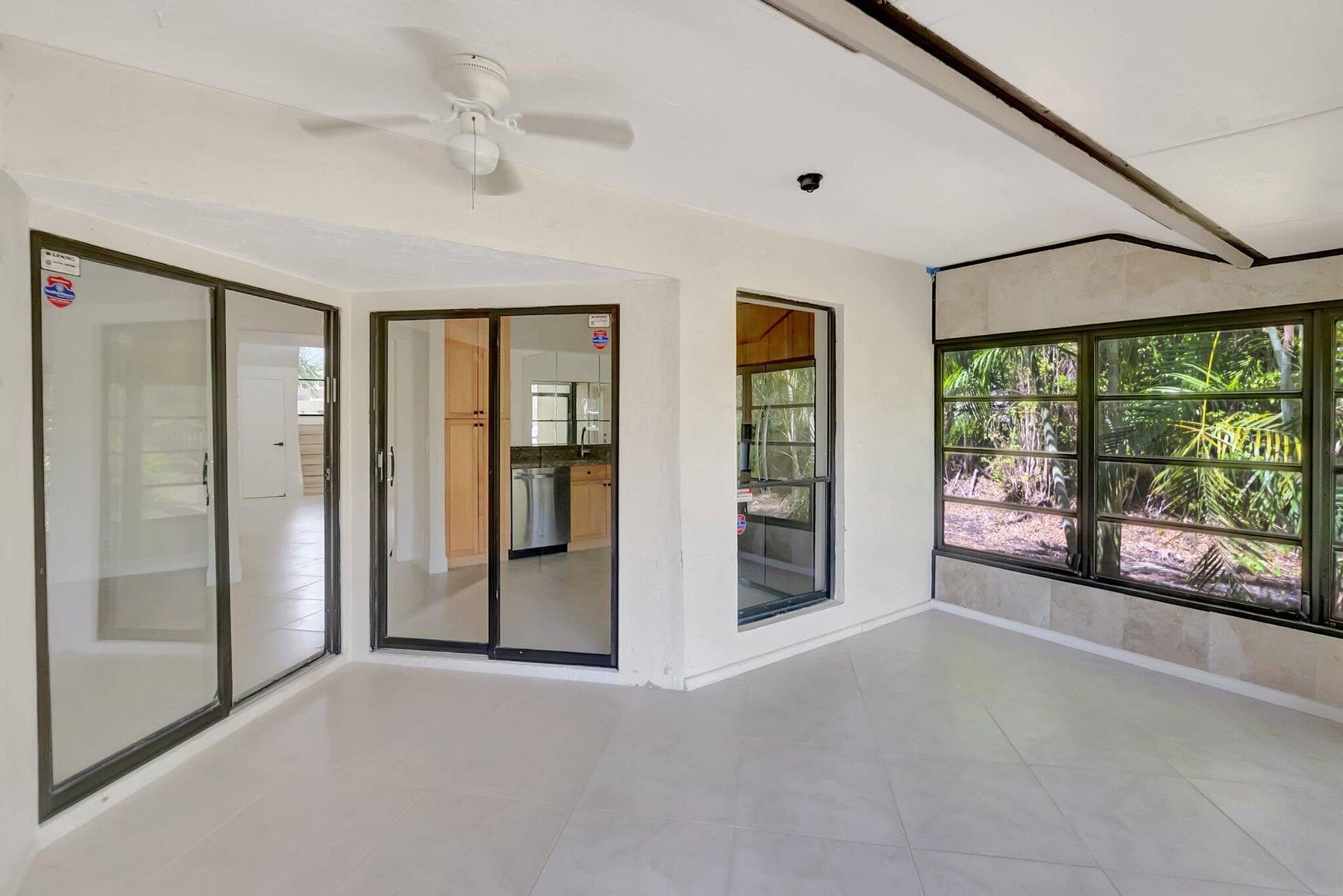 Enclosed sunroom featuring large-format tile flooring, multiple sliding glass doors, neutral wall finishes, and a ceiling-mounted fan