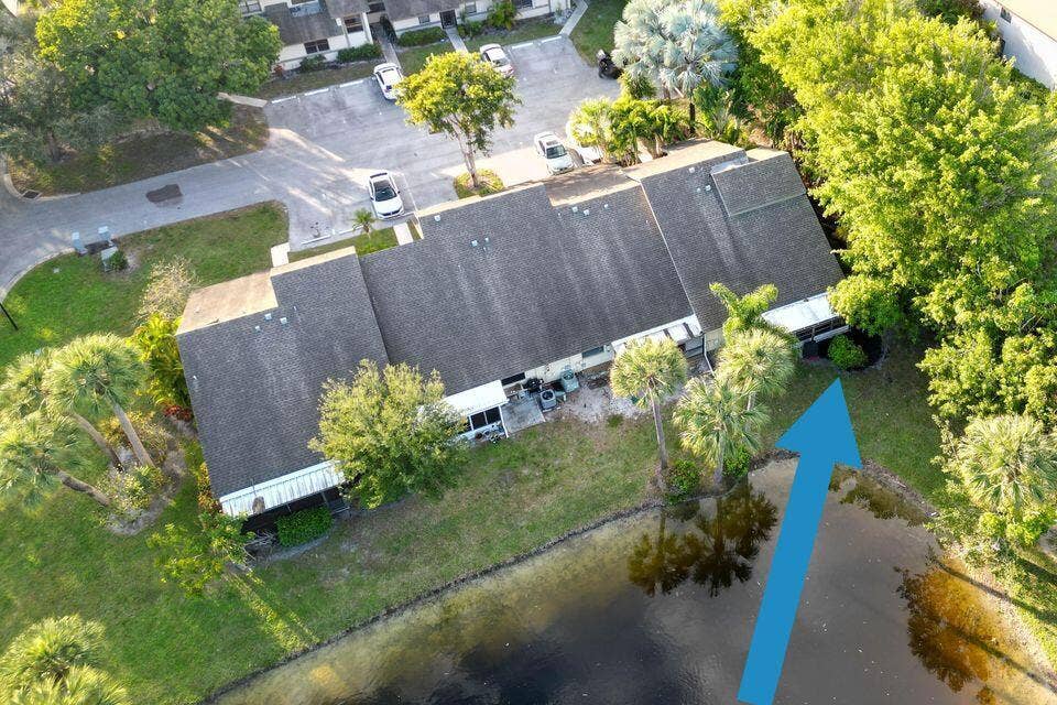 Aerial perspective of a multi-unit property featuring a shingled gable roof, screened-in porch area, and mature landscaping, situated along a pond