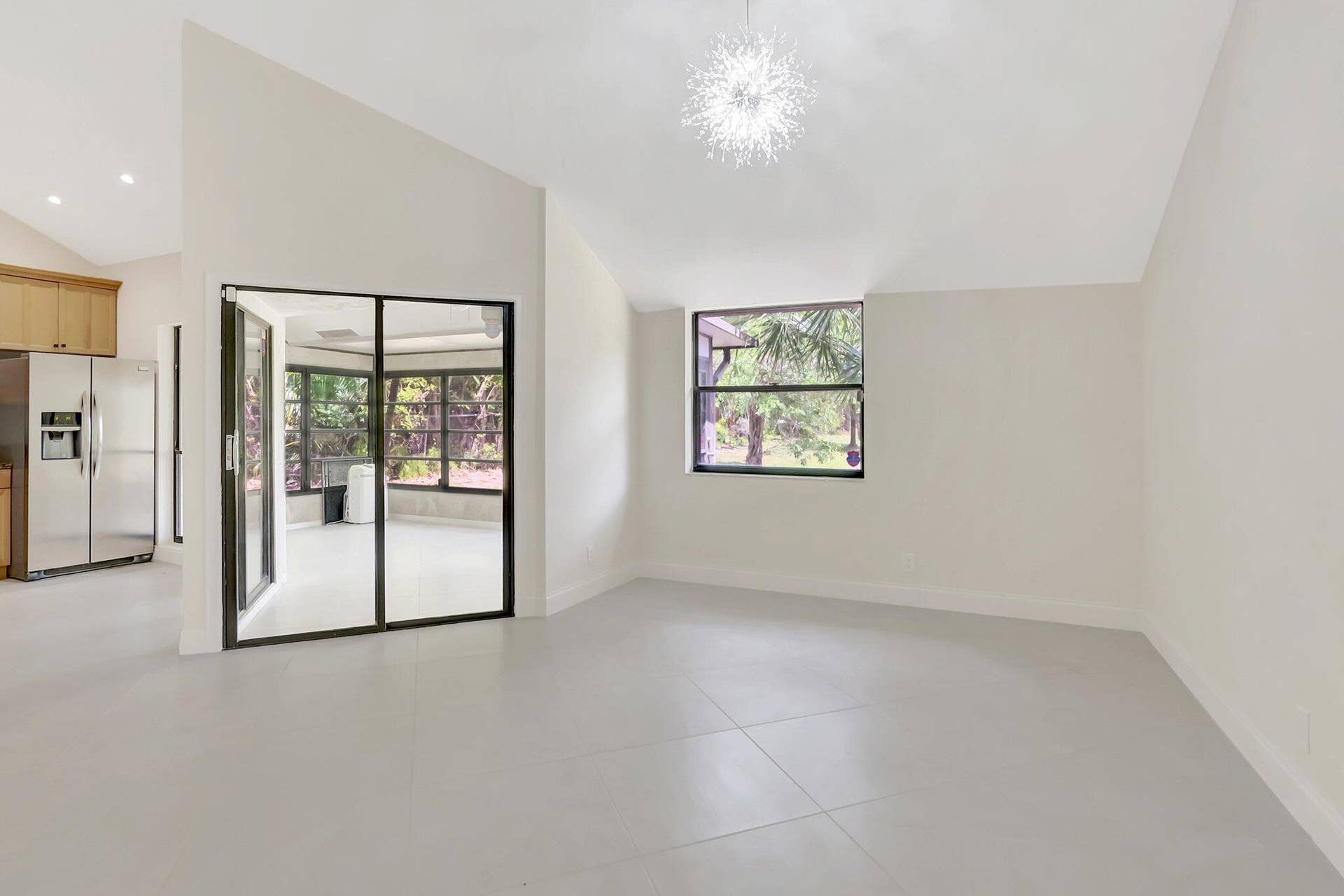 Vaulted ceilings, large-format tile flooring, a statement starburst chandelier, and sliding glass doors with black frames