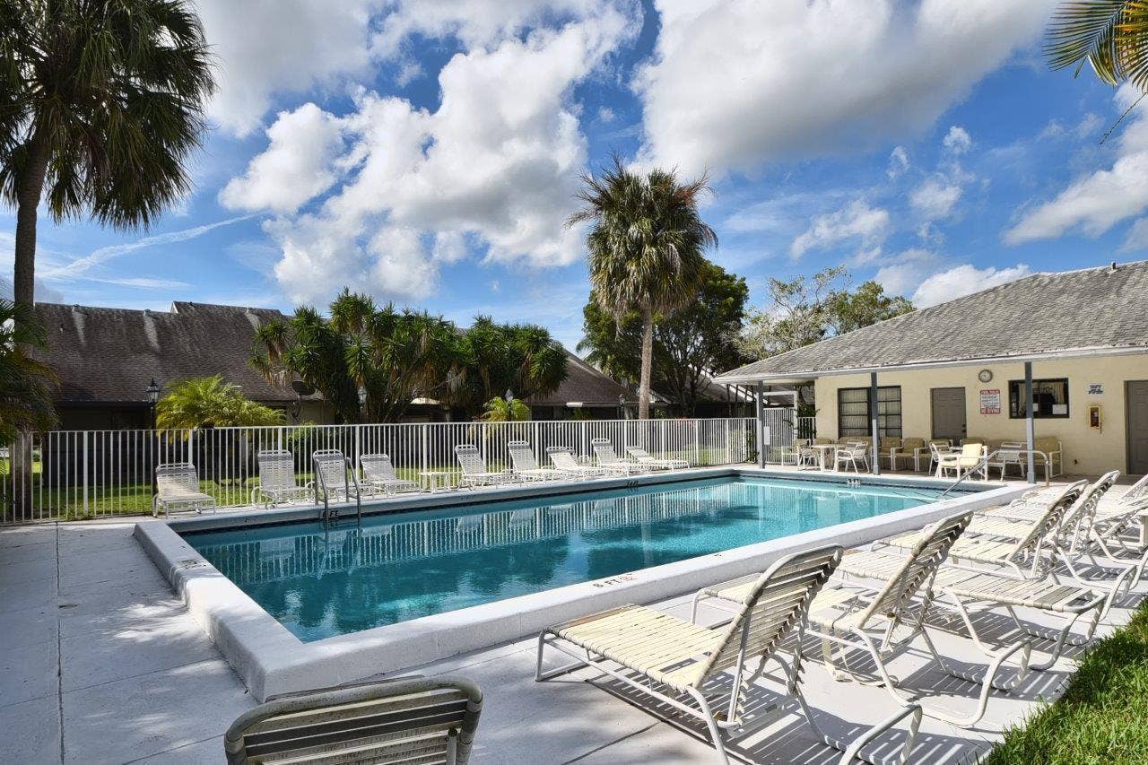 In-ground swimming pool featuring a concrete deck, perimeter fencing, and mature palm trees