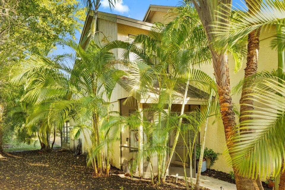 Multi-story exterior featuring light-toned stucco siding, a screened-in porch, and established palm landscaping