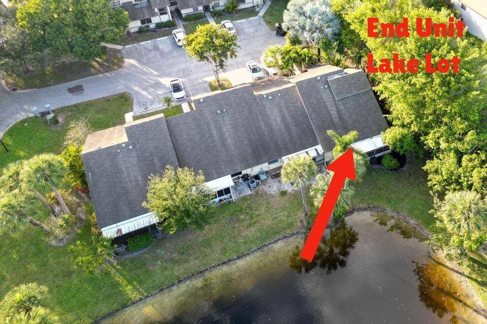 Aerial perspective of an end-unit townhouse featuring a shingled roof, a covered patio, and a lot situated on a lake