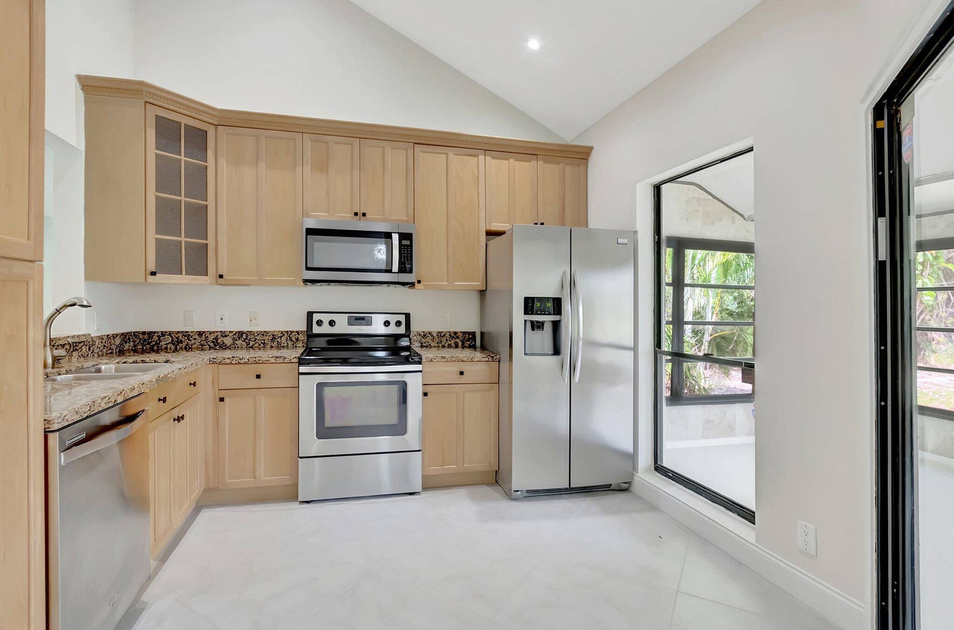 Kitchen featuring light-finish cabinetry, stone-surfaced countertops, stainless steel appliances, a vaulted ceiling, and tile flooring