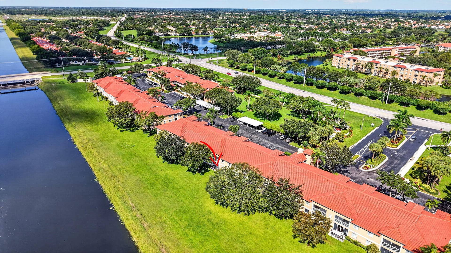 Aerial perspective featuring terracotta-style roofing, paved parking facilities, mature landscaping, and waterfront grounds