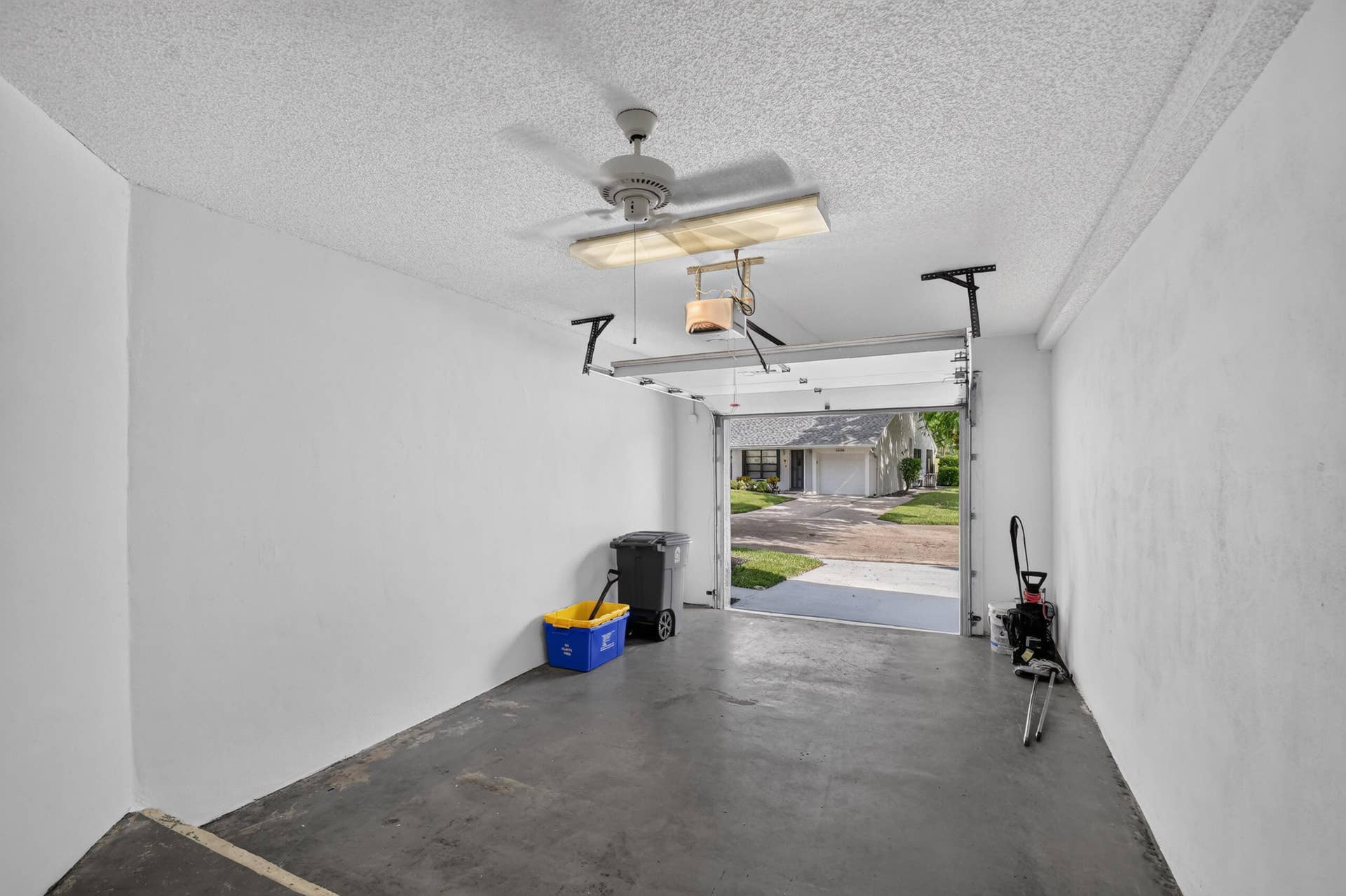 Enclosed garage featuring painted interior walls, concrete flooring, a ceiling-mounted light fixture, and an automated overhead garage door opener