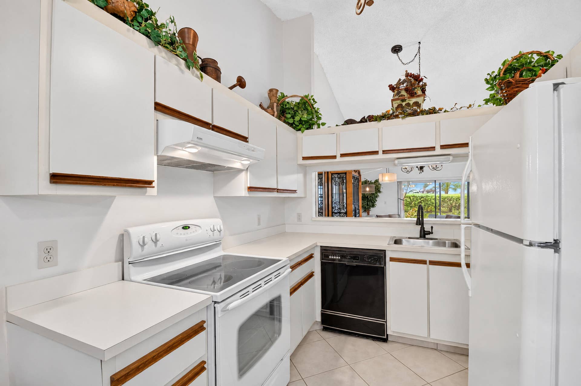 Kitchen featuring white cabinetry with wood trim, solid surface countertops, vaulted ceiling, tile flooring, and a pass-through window
