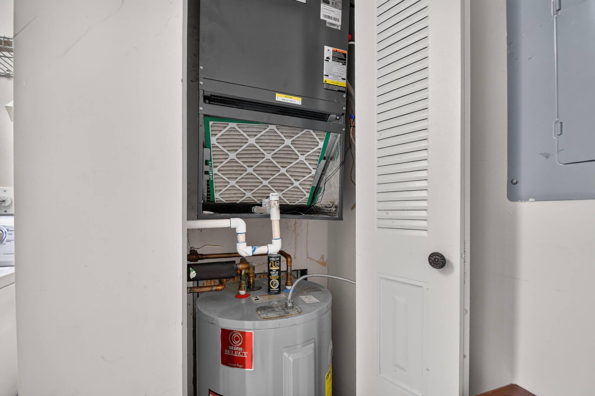 Utility closet housing an HVAC air handler unit and a water heater with louvered door access