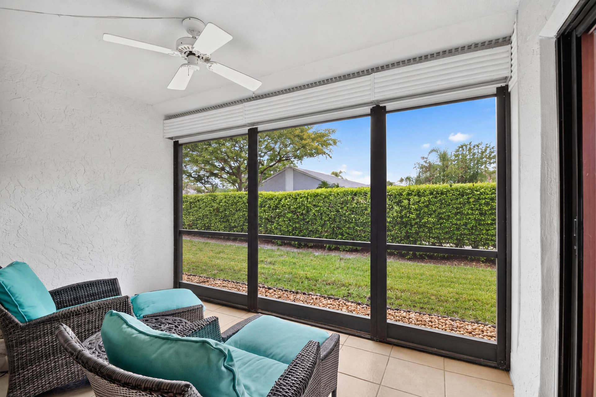 Enclosed lanai featuring a tile floor, ceiling fan, and large screened panels overlooking a landscaped yard