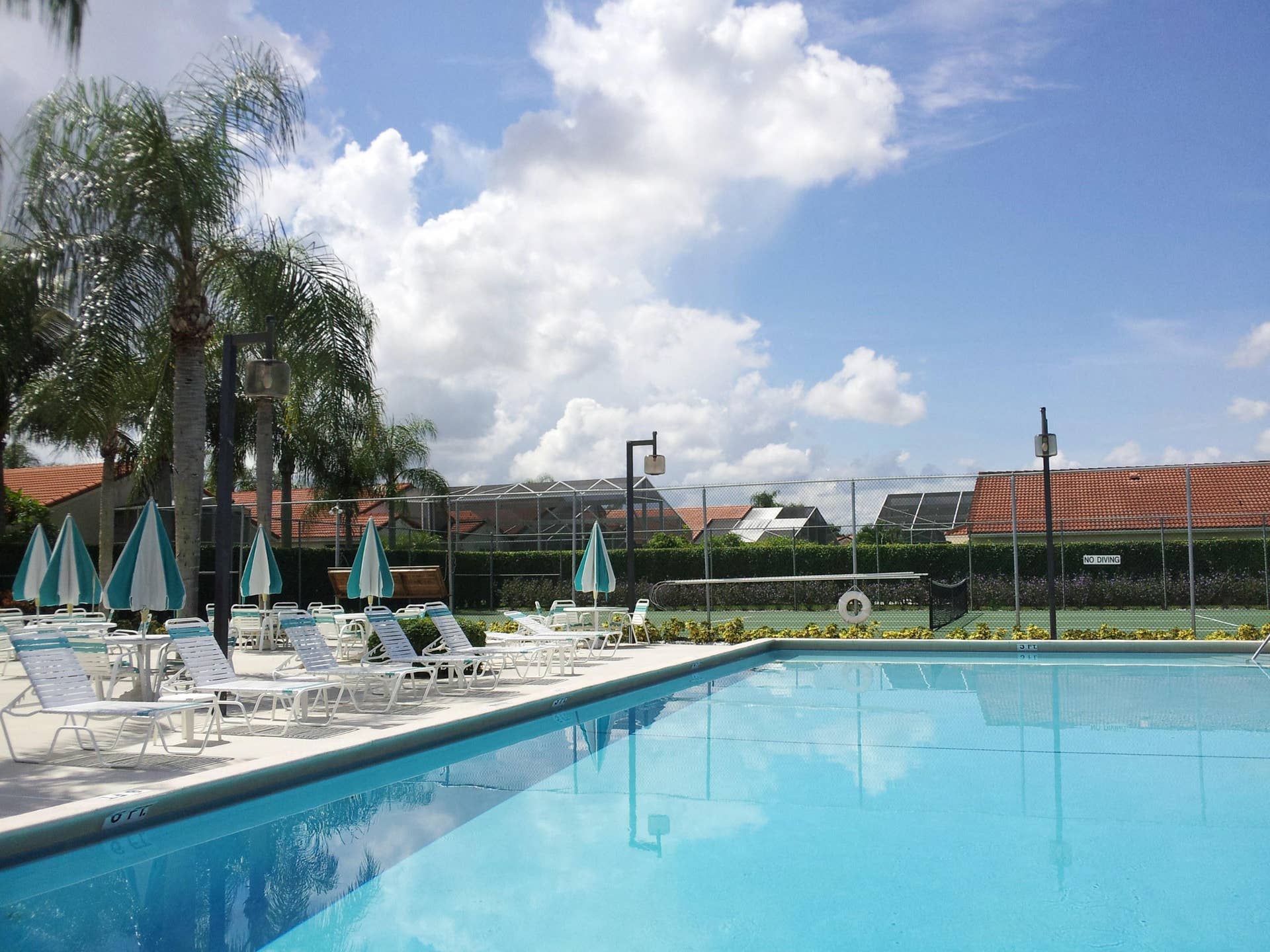 Swimming pool with concrete decking, perimeter fencing, and hard-surfaced tennis court