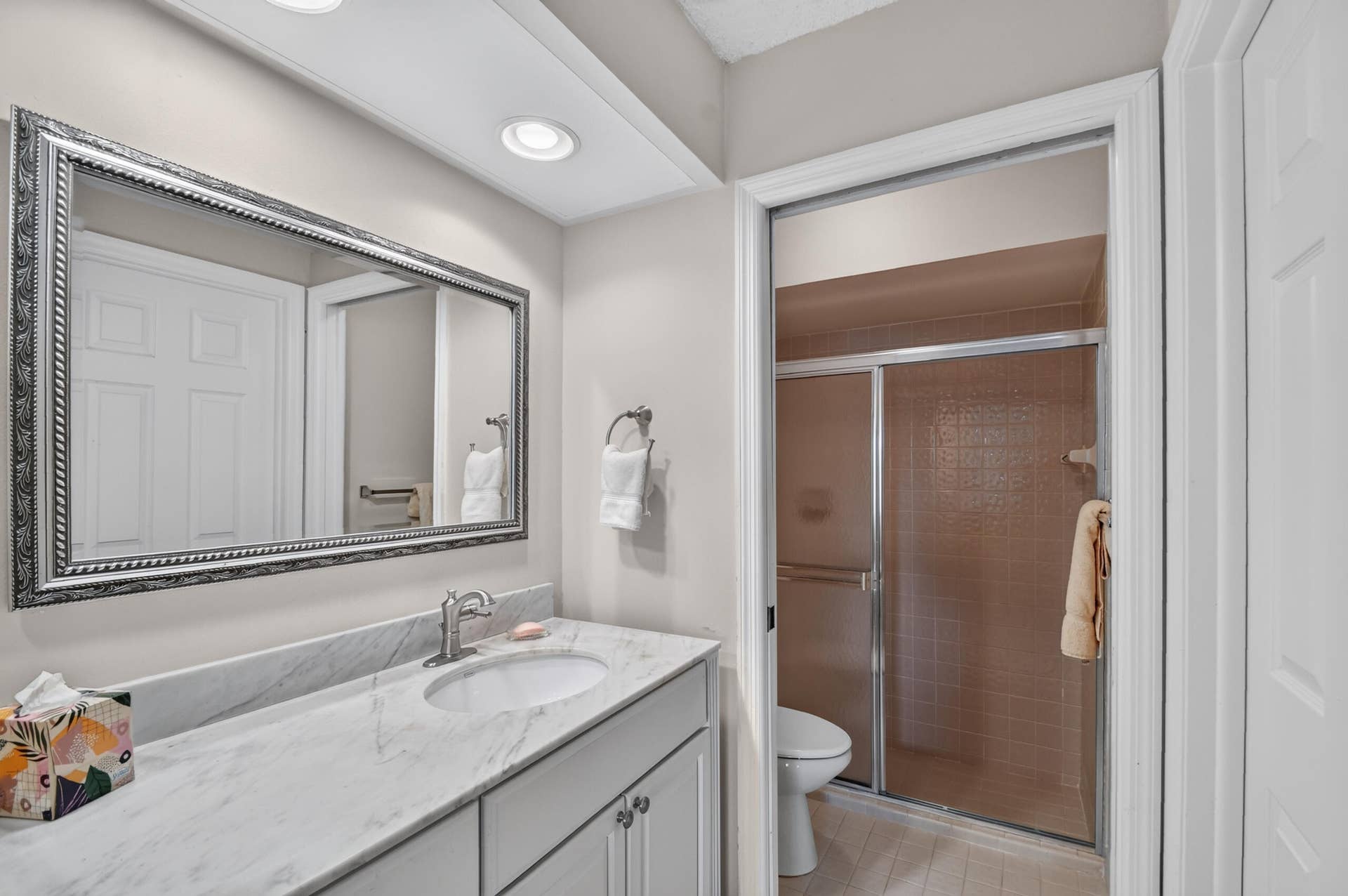 Bathroom vanity featuring a stone-surface countertop, an integrated undermount sink, polished chrome faucet, and a large framed wall mirror recessed beneath integrated ceiling lighting