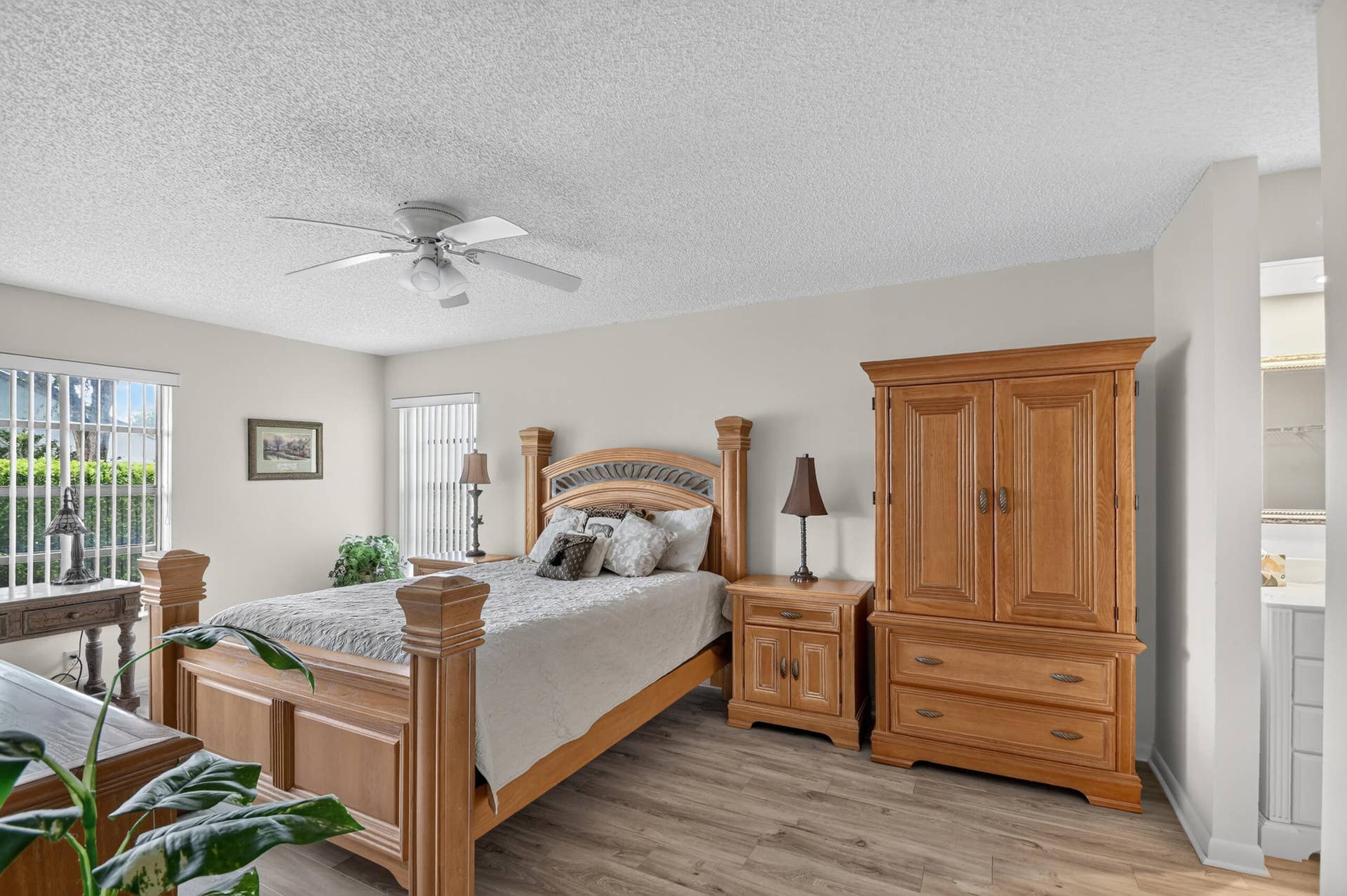 Wood-finish flooring, dual windows with vertical blinds, and a ceiling fan with light fixture
