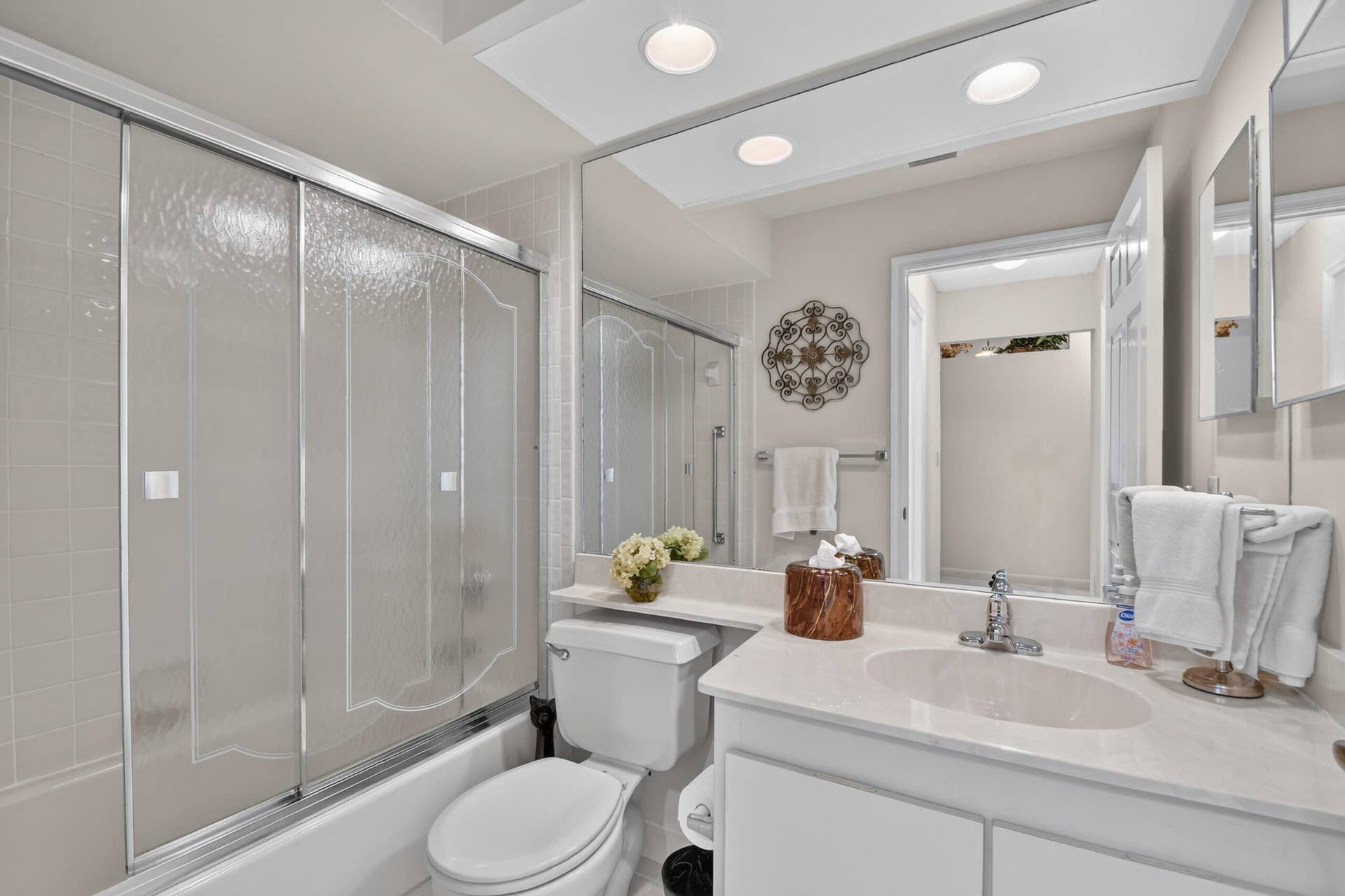 Bathroom featuring a vanity with a stone countertop, an integrated oval sink, textured glass shower doors, and a full-width wall mirror with recessed lighting